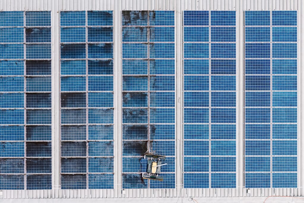 Drone view of a commercial array mid-clean: cleaned rows on the right, still to do on the left