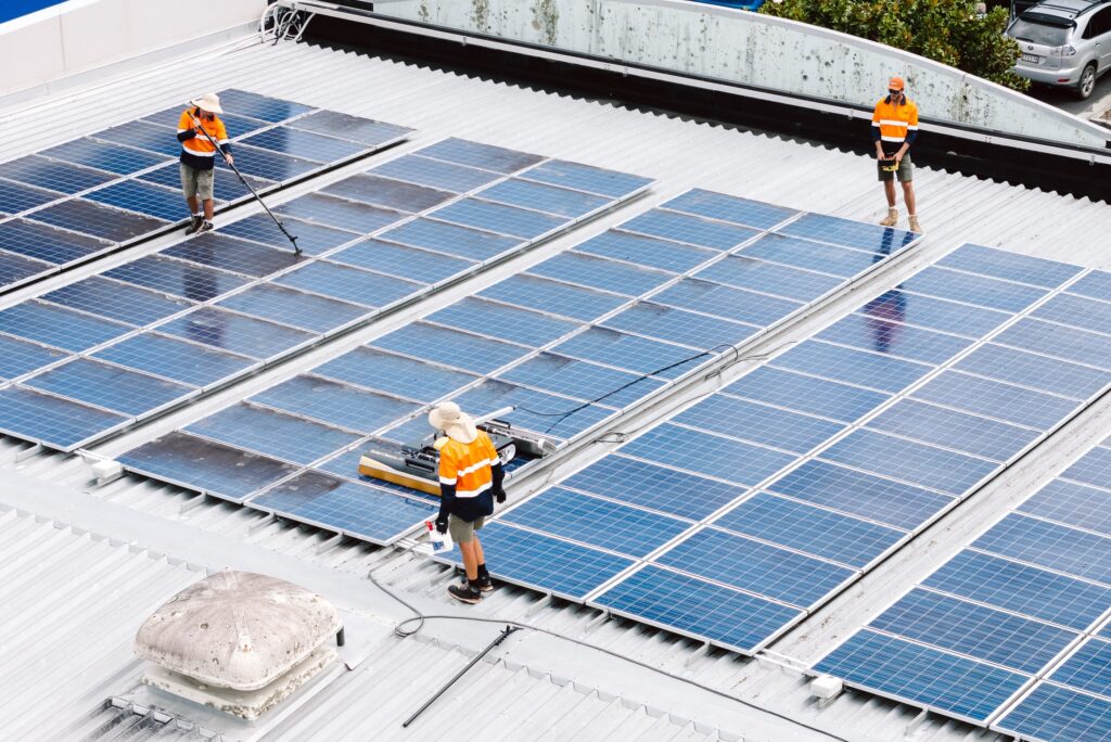 Eco Shine Solar crew cleaning a commercial rooftop array with water-fed poles and the robot