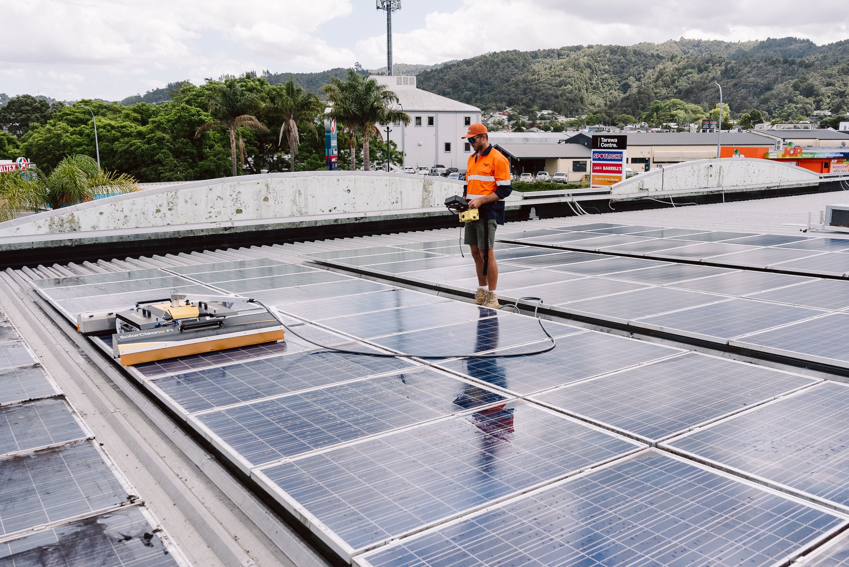 Technician guiding a robotic solar panel clean on a commercial building roof